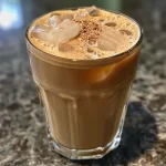 A close-up view of a glass filled with iced coffee, showcasing ice cubes and a creamy top.