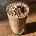 Close-up view of a High Protein Mocha Madness drink in a glass, with toppings of toasted coconut flakes and almonds.