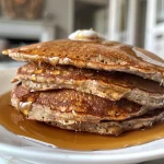 Close-up of fluffy high protein pancakes stacked on a plate with syrup drizzle.