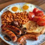 Close-up of a hearty Full English Breakfast featuring sausages, eggs, toast, tomatoes, and mushrooms.