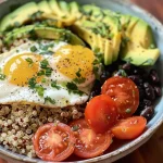 Close-up of a colorful protein breakfast bowl with quinoa, eggs, avocado, black beans, and diced tomatoes.