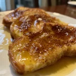 A close-up side view of Crème Brûlée French Toast topped with a caramelized sugar crust.