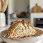 A close-up side view of a golden-brown loaf of sourdough bread, showcasing its crusty exterior.