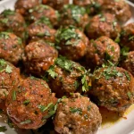 A close-up side view of juicy Middle Eastern spicy meatballs glistening with sauce.