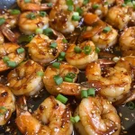 Close-up of juicy honey garlic shrimp garnished with green onions and sesame seeds.