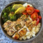 A close-up side view of a colorful lemon herb chicken protein bowl with roasted vegetables and mashed cauliflower.