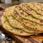 Close-up of golden-brown flatbreads stacked on a wooden board.