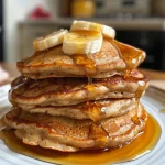 A stack of fluffy banana oat pancakes topped with fresh berries and a drizzle of maple syrup.