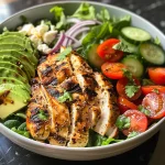 A vibrant grilled chicken and avocado salad bowl with mixed greens, cherry tomatoes, and cucumbers.