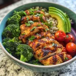 A close-up side view of a colorful grilled chicken veggie bowl featuring chicken, broccoli, red bell pepper, and cherry tomatoes.