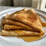 Close-up side view of fluffy high protein cinnamon crepes stacked on a plate, showcasing a golden-brown color.