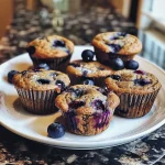 Close-up side view of homemade blueberry protein muffins, featuring a golden-brown top and visible blueberries.