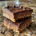 Close-up of no-bake protein bars with a glossy chocolate topping and a sprinkle of mini chocolate chips.