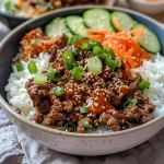 Close-up view of a vibrant Korean Beef Rice Bowl topped with sesame seeds and sliced scallions.