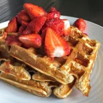 Close-up view of high-protein gluten-free strawberry oat waffles topped with strawberry sauce.