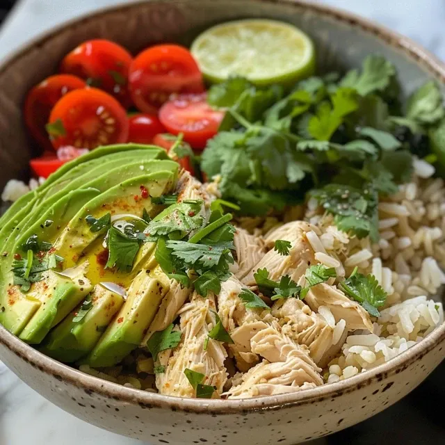 Close-up view of a rice bowl with chicken, avocado, and colorful toppings.
