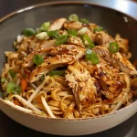 Close-up of juicy chicken noodles with colorful vegetables.