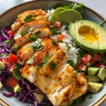 Close-up view of a Baja Fish Taco Bowl featuring crispy white fish, vibrant slaw, and a creamy chipotle-lime sauce.