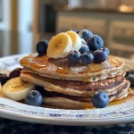 Golden brown banana blueberry pancakes stacked high, topped with fresh blueberries.