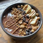 Close-up of a chocolate peanut butter smoothie bowl topped with sliced bananas and granola.