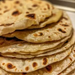 Close-up of a stack of freshly made flour tortillas showing a golden-brown surface.