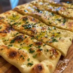 Close-up view of golden-brown garlic flatbreads arranged on a wooden board.