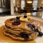 Fluffy pancakes stacked with blueberries and banana slices on top.