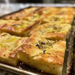 Close-up view of soft, golden-brown gluten-free focaccia with visible rosemary.