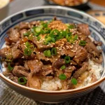 A close-up view of a Gyudon beef rice bowl with tender slices of beef and glossy sauce.