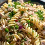 Close-up view of a vibrant tuna pasta salad with rotini, peas, and chopped vegetables.