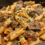 Close-up view of a bowl of One-Pot Zesty Steak Pasta topped with fresh herbs.
