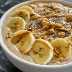 Close-up of a peanut butter banana smoothie bowl topped with sliced bananas and drizzled peanut butter.