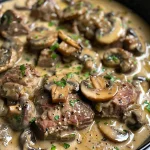 Close-up view of juicy beef in creamy mushroom sauce with mushrooms and garnishes.
