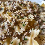 A close-up view of creamy Parmesan garlic beef bowtie pasta garnished with parsley.
