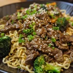 Close-up view of honey garlic beef noodles with sliced beef and broccoli.