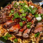 Close-up view of a bowl of spicy Korean beef noodles with tender flank steak and green onions.