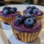 ['Close-up of three blueberry protein cups, showcasing their creamy texture and vibrant blueberries.', 'Side view of delicious blueberry protein cups filled with cottage cheese and topped with fresh blueberries.', 'Juicy, colorful blueberry protein cups displayed on a wooden surface, highlighting the ingredients.', 'A detailed view of blueberry protein cups, emphasizing the chunks of frozen blueberries and smooth texture.']