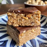 ['Close-up view of Cashew Vanilla Snack Bars with a glossy surface.', 'Side view of a stack of homemade Cashew Vanilla Snack Bars.', 'Delicious Cashew Vanilla Snack Bars with dark chocolate drizzled on top.', 'Raw Cashew Vanilla Snack Bars arranged on a wooden cutting board.']