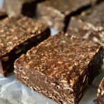 ['Close-up of chocolate espresso protein oat bars displaying layers of chocolate and oats.', 'Side view of delicious chocolate espresso oat bars with a glossy chocolate coating.', 'Tasty chocolate espresso protein oat bars stacked on a wooden board.', 'Appetizing chocolate espresso bars showcasing a combination of oats and chocolate.']
