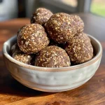 ['Close-up side view of Chocolate Espresso Tahini Energy Balls, showcasing their rich texture.', 'A row of Chocolate Espresso Tahini Energy Balls, highlighting their glossy chocolate coating and sprinkle of chia seeds.', 'Detailed view of a Chocolate Espresso Tahini Energy Ball, revealing chocolate chips and tahini ingredients.', 'Side shot of multiple Chocolate Espresso Tahini Energy Balls piled on a plate, looking moist and inviting.']