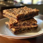 ['Close-up side view of dark chocolate, date, and oatmeal bars on a plate.', 'Juicy dark chocolate bars with oats and dates, displayed on a wooden table.', 'A delicious slice of dark chocolate and date oatmeal bar resting on a white dish.', 'Side view image of homemade dark chocolate and date oatmeal bars garnished with oats.']