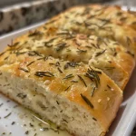 ['A close-up view of a crusty homemade rosemary bread loaf, showcasing its golden-brown crust and fluffy interior.', 'Side view of freshly baked rosemary bread with visible herbs and a crispy crust, resting on a wooden board.', 'Juicy homemade rosemary bread displayed with a rich texture and fresh rosemary sprigs beside it.', 'Detailed image of a loaf of rosemary bread, highlighting its inviting crust and soft, airy inside.']