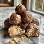 ['Close-up view of glossy No-Bake Peanut Butter Balls on a wooden surface.', 'Side view of multiple peanut butter balls, highlighting their creamy texture.', 'Delicious-looking No-Bake Peanut Butter Balls with a shiny exterior, arranged neatly.', 'A handful of No-Bake Peanut Butter Balls showcasing their golden-brown color.']