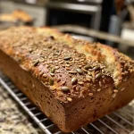 ['Close-up side view of a golden-brown, multi-seed bread with a crusty exterior and a soft interior.', 'Juicy, delicious no-knead multi-seed bread displayed on a wooden board, highlighting its nutty seed toppings.', 'Side view of freshly baked multi-seed bread, showcasing its texture and variety of seeds on top.', 'A vibrant close-up of no-knead multi-seed bread, with visible sunflower, pumpkin, and sesame seeds adorning the crust.']