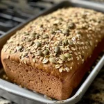 ['Close-up side view of a loaf of No Knead Seeded Oat Bread with a golden crust and visible seeds.', 'Side view of freshly baked No Knead Seeded Oat Bread showing a textured crust and sprinkled seeds.', 'Juicy No Knead Seeded Oat Bread displayed in a side view, highlighting its rustic appearance and seed toppings.', 'Detailed side view of a delicious No Knead Seeded Oat Bread with an array of pumpkin and sunflower seeds.']