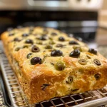 ['Close-up of freshly baked olive bread, showcasing its golden crust and visible olive pieces.', 'Side view of a loaf of olive bread, displaying a soft interior and rustic crust.', 'Juicy slice of olive bread with chopped olives peeking through, placed on a wooden surface.', 'A freshly cut piece of olive bread, highlighting its texture and gourmet ingredients.']