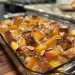 ['Close-up of a Peach French Toast Bake topped with sliced almonds.', 'Side view of Peach French Toast Bake showing golden crust and peach slices.', 'Juicy Peach French Toast Bake with a sprinkle of almonds and cinnamon.', 'Deliciously baked Peach French Toast with visible peach slices and almond topping.']