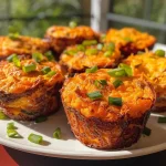 ['Close-up view of golden-brown savory sweet potato muffins with visible green onions and jalapeños.', 'Side view of moist sweet potato muffins featuring a crumbly texture and colorful toppings.', 'Juicy savory muffins made with sweet potatoes, cheese, and herbs, placed on a rustic surface.', 'A plate of freshly baked sweet potato muffins, showcasing their fluffy interior and toppings.']
