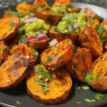 ['Close-up of golden-brown Sweet Potato Bites garnished with cilantro and served with guacamole.', 'Side view of crispy Sweet Potato Bites arranged on a plate with a bowl of Mexican hot sauce.', 'Juicy Sweet Potato Bites topped with minced red onion and corn, displayed with a sauce on the side.', 'An appetizing shot of Sweet Potato Bites highlighting their texture, accompanied by avocado sauce.']