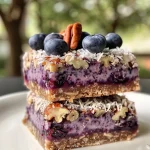 ['Close-up side view of Vegan Blueberry Cheesecake Bars with a creamy layer and blueberries on top.', 'A slice of Vegan Blueberry Cheesecake Bars featuring a crumbly crust and vibrant blueberries.', 'Side image of vegan dessert bars displaying a creamy cheesecake layer garnished with fresh blueberries.', 'Detailed view of Vegan Blueberry Cheesecake Bars showcasing a coconut crust and blueberry topping.']